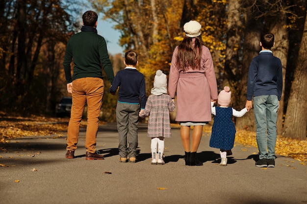 Große Familie mit vier Kindern, die Händchen halten und im Herbstpark auf der Straße stehen, Rückansicht.