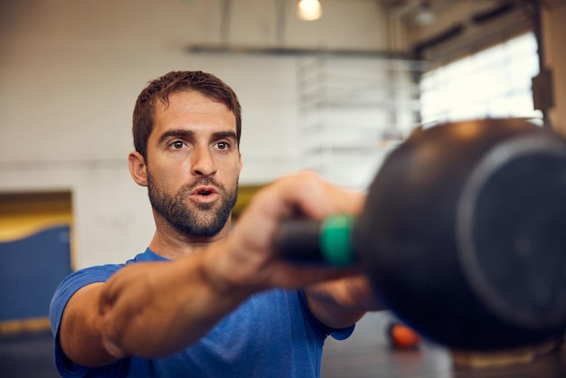 Große Fortschritte bei der Erreichung seiner Ziele gemacht Schnappschuss eines gutaussehenden jungen Mannes, der im Fitnessstudio mit einer Kettlebell trainiert