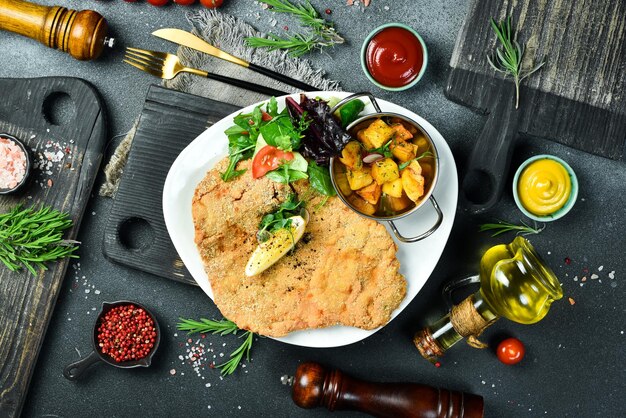 Große gebratene Hühnerschnitzel mit Gemüse in einem Teller auf einem schwarzen Steinhintergrund Foto von Essen