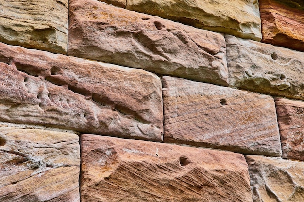 Große geformte Steinsteinmauer mit Erdtonfarben und rustikalem rotem abstrakten Hintergrund