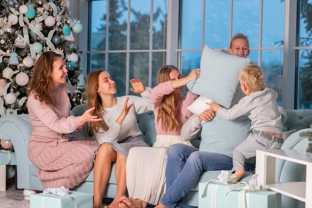 Große glückliche Familie mit vielen Kindern, die an Heiligabend eine Kissenschlacht unter dem Weihnachtsbaum haben