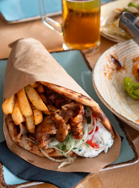 Große griechische Gyros mit Fleisch, Pommes Frites, Tomaten, Zwiebeln in der Pita, mit einem Glas Bier in der Hand.