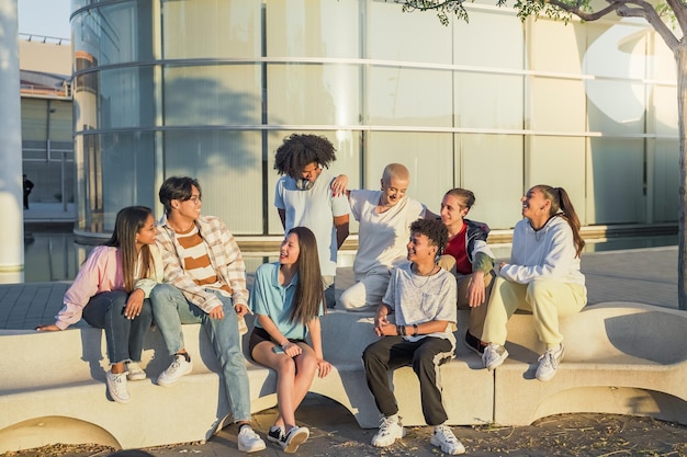 Große Gruppe glücklicher Teenagerfreunde, die sich auf einer Bank auf der Straße des Studentencampus unterhalten