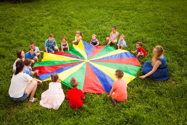 Große Gruppe Kinder, die Fallschirmspiel auf dem grünen Feld spielen