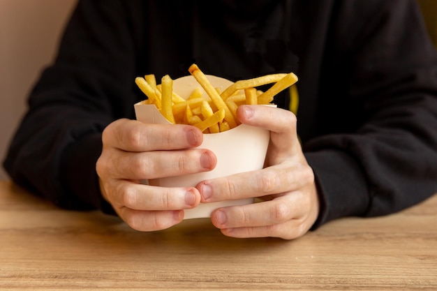 Große Hände eines Mannes in einem schwarzen Hoodie mit Vitiligo, um Pommes Frites in Papierverpackungen zu halten