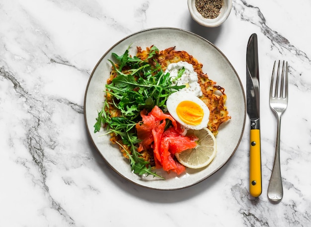 Große Kartoffelrösti mit Eierrucola, Lachs und griechischer Joghurtsauce auf hellem Hintergrund, Draufsicht Köstliches Essen