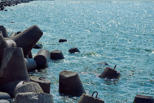 Große konkrete Wellenbrecher-Tetrapoden in der Nähe des lebhaften Aquamarin-Meeres mit grellem Sonnenlicht auf der Wasseroberfläche, Nahaufnahme, Makro. Blöcke und Steine zum Schutz der Küste vor Sturm, schöne Meereslandschaft