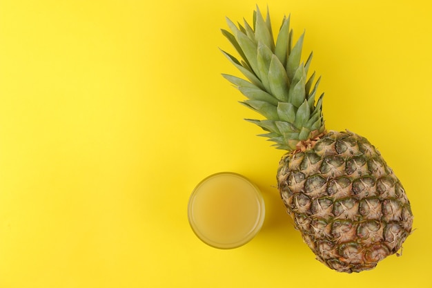 Große reife Fruchtananas und Ananassaft auf einem leuchtend gelben Tisch. Sommer. Ansicht von oben.