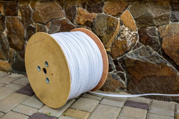 Große Rolle des weißen industriellen elektrischen Kabels auf großer hölzerner Spule draußen