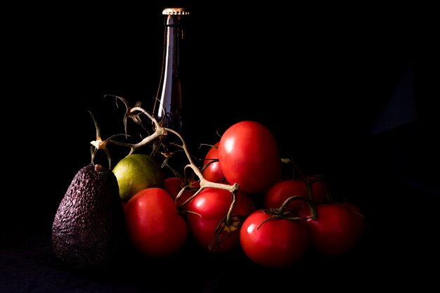 Große rote und reife Tomaten mit Kalkavocado und Flasche Bier auf Schwarzem