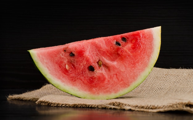 Große Scheibe der reifen Wassermelone auf Sackleinen, schwarzer Hintergrund