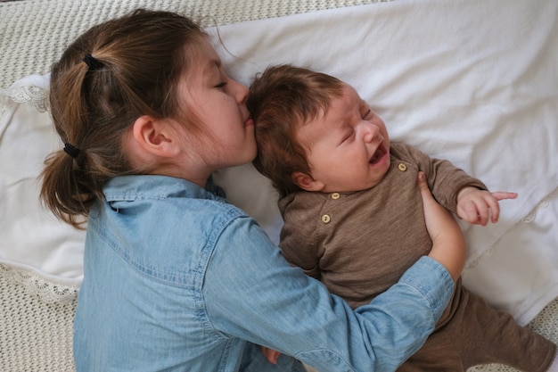 Große Schwester küsst kleines weinendes Baby auf der Couch. Glückliche Familie. Zu Hause. Liebe. Süss. Zärtlichkeit. Große Schwester. Zeitlupe