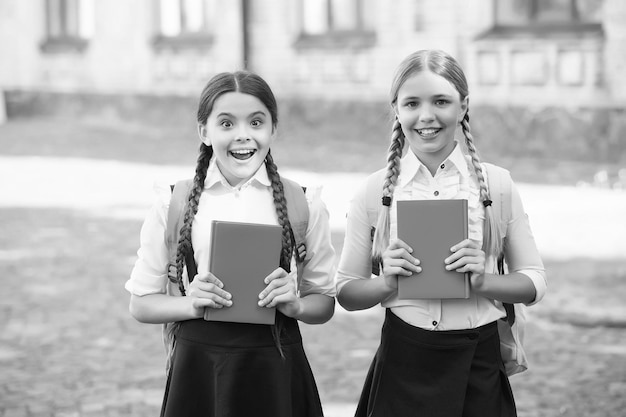 Foto große überraschung für sie schulmädchen, die zusammen ein fach lernen, haben spaß beim lernen glückliche mädchen in schuluniform überraschten teenager-studenten mit rucksack halten copybook-ausbildung in der grundschule