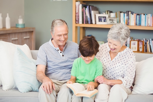Großeltern, die Enkel beim Lesebuch im Wohnzimmer unterstützen