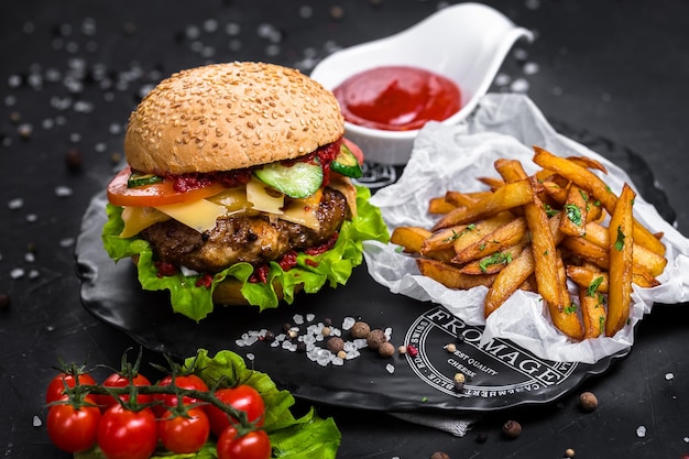 großer Burger mit Fleischkotelett, mit roter Ketchup-Sauce in weißem Teller, Schüssel, Pommes Frites oder Idaho,