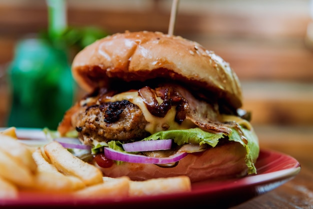 Großer Cheeseburger und Pommes auf einem Teller.