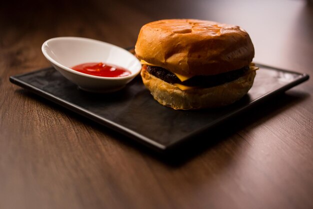 Großer frischer Burger mit Sauce und Pommes auf schwarzem Teller Amerikanisches klassisches Burger-Menü