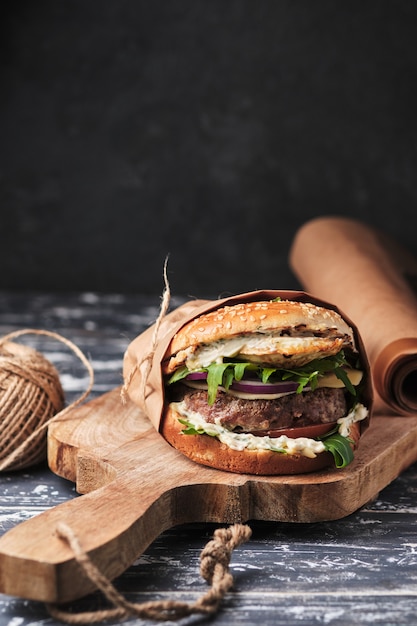 Großer gegrillter Burger mit Gemüse auf einem Holzbrett