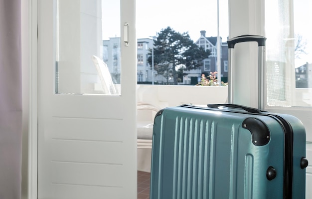 Großer grüner Koffer bleibt im Zimmer im Hotel in der Nähe von Fenster oder Balkon mit Sonnenlicht