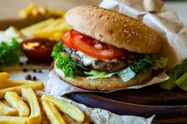 großer leckerer Burger auf einem Holztisch und Pommes. Köstlicher Burger mit Rindfleisch-Tomaten-Käse und Salat