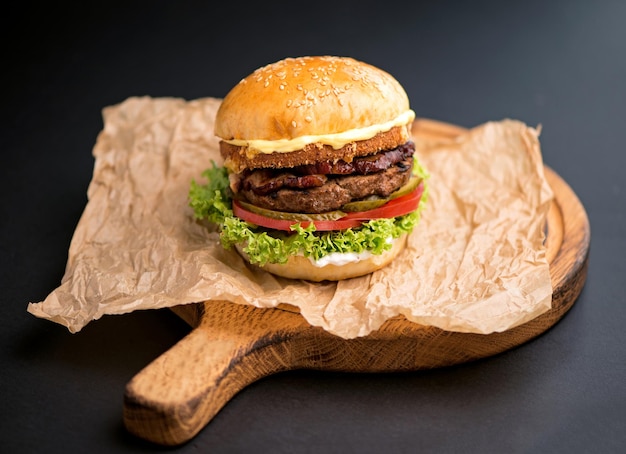 Großer leckerer Burger mit Rinderkotelett auf schwarzem Hintergrund