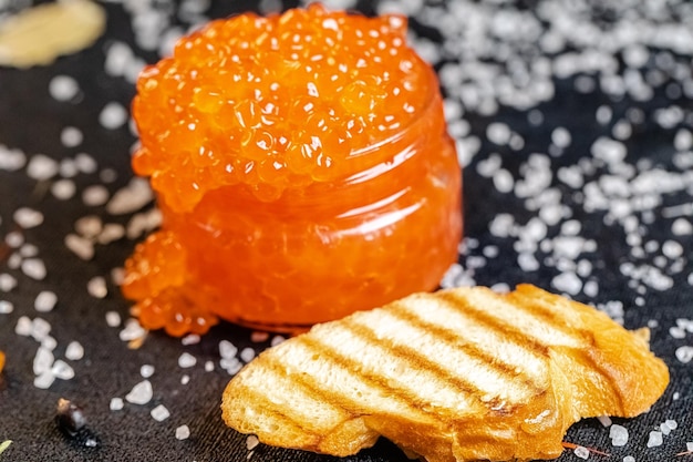 großer roter Kaviar in einem Glas, mit einem Löffel aufheben, liegt auf Pergament, neben einem Brotlaib u