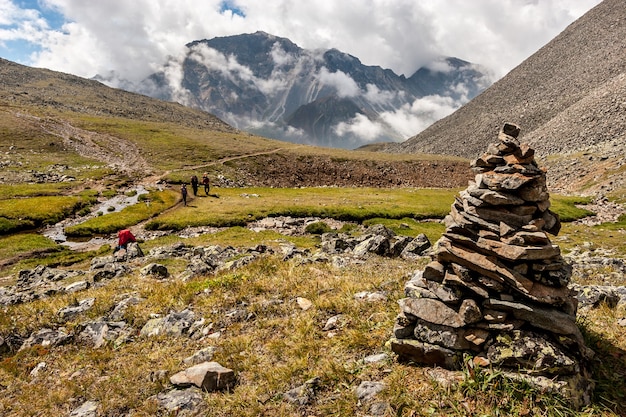 Großer Steinhaufen im Vordergrund der Berglandschaft mit niedrigen weißen Wolken über den Bergen