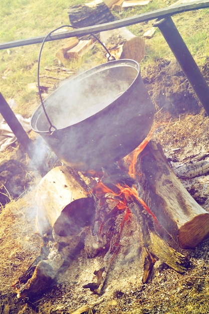 Großer Topf über dem Lagerfeuer mit Rauch und Brennholz, Fotofilter