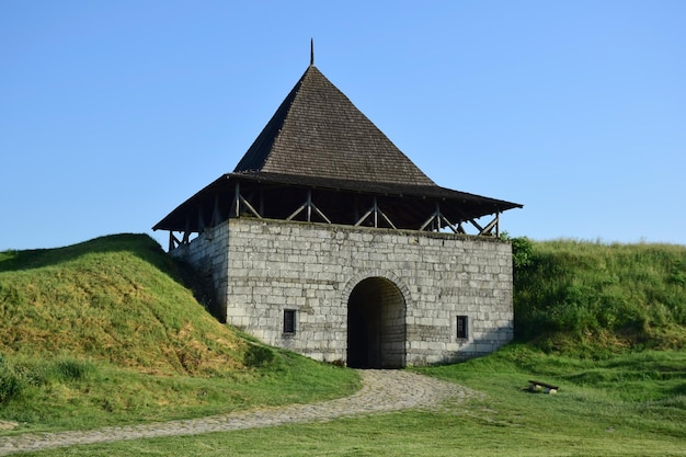 Großer turm einer mittelalterlichen steinfestung mit gewölbtem eingang und erdwällen an den seiten