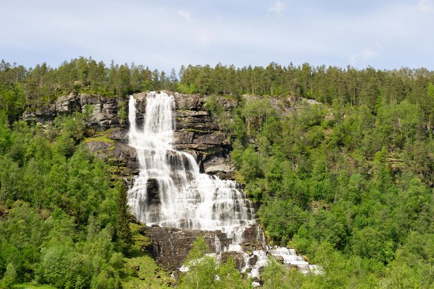 Großer Wasserfall, der sich in den Bergen erhebt, umgeben von grünen Bäumen in Norwegen