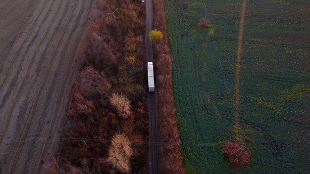 Großer weißer Lastwagen und weißes Auto, das eine unbefestigte Straße zwischen landwirtschaftlichen Feldern auf dem Land fährt