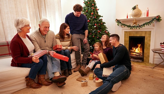 Großes Familienweihnachten und Geschenk im heimischen Wohnzimmer zum Feiern, Glück und Zusammensein Glückliche Großeltern und Kinder der Familie mit Geschenken und Box mit Liebesurlaub oder Lounge