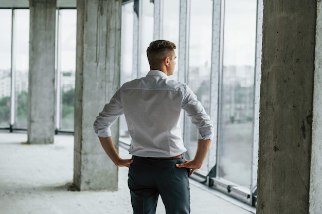 Großes Fenster Junger Mann in formeller Kleidung arbeitet drinnen am Bau