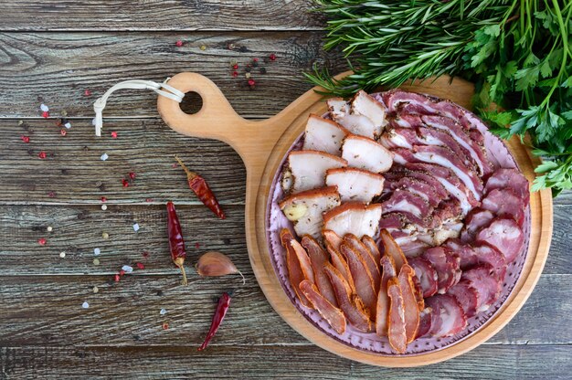 Großes Fleischset. Hausgemachte geräucherte Schweinswurst, gesalzener Speck, gehackte Basturma-Scheiben auf einem Holzbrett mit Gewürzen und Kräutern. Flach liegen. Die Draufsicht