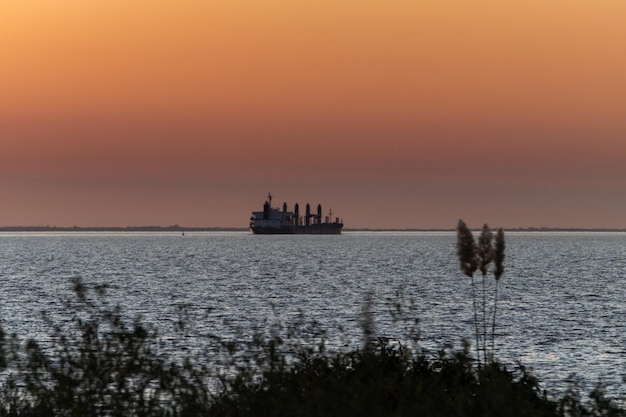 Großes Frachtschiff während eines tieforangefarbenen Sonnenuntergangs am Uruguay River Colonia Uruguay