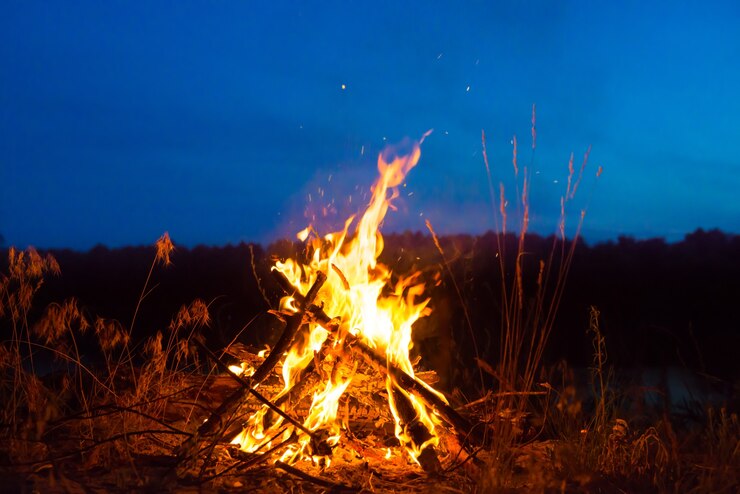 Großes Lagerfeuer nachts im Wald unter dunkelblauem Nachthimmel mit vielen Sternen