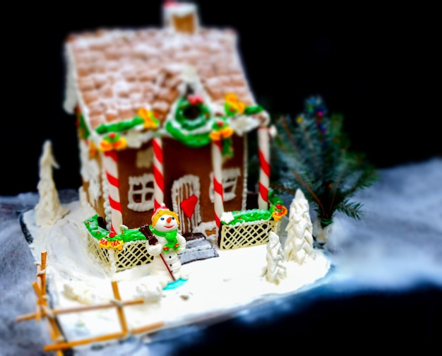 Großes Lebkuchenhaus, ein Weihnachtsbaum und ein Zuckermastix-Schneemann auf dunklem Hintergrund. Mockup für saisonale Angebote und Urlaubspostkarte