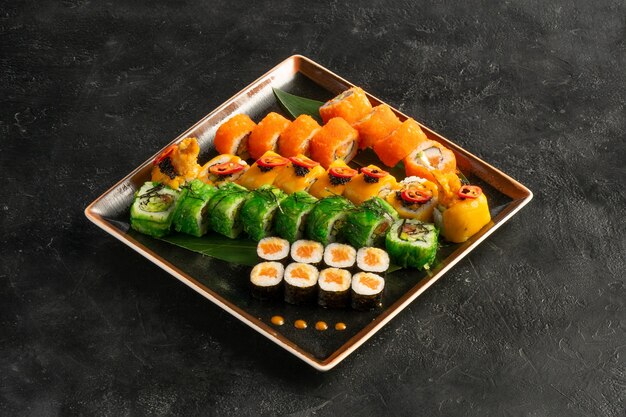 Großes Maki-Sushi-Set mit einer abwechslungsreichen Auswahl japanischer Brötchen in einem quadratischen Teller auf einem schwarzen Steintisch