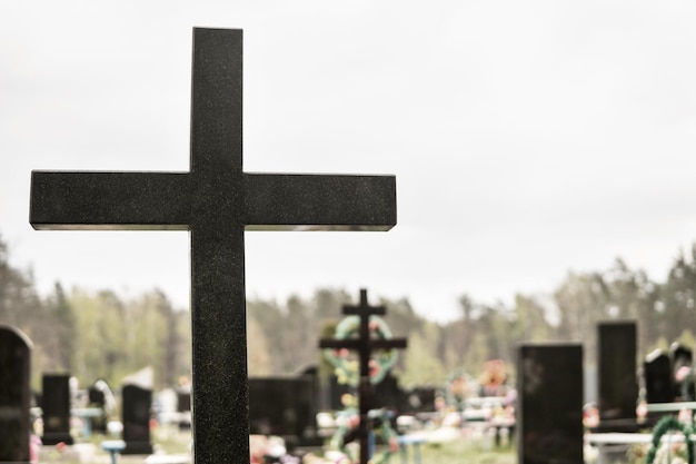 Großes Marmorkreuz auf dem Hintergrund eines verschwommenen christlichen Friedhofs