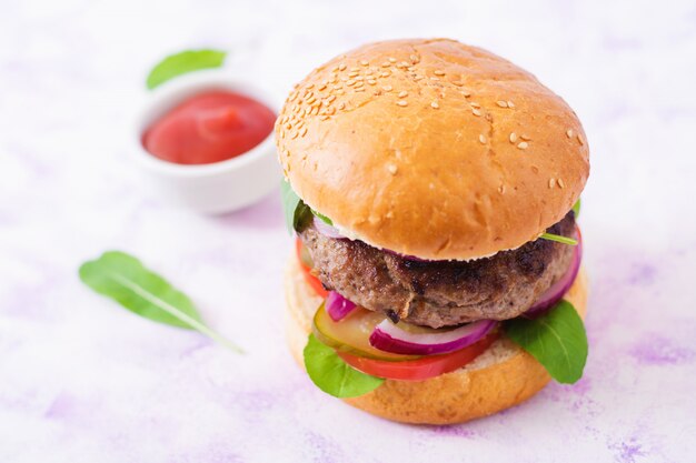 Großes Sandwich - Hamburgerburger mit Rindfleisch, Essiggurken, Tomate und roten Zwiebeln auf einem hellen Hintergrund.