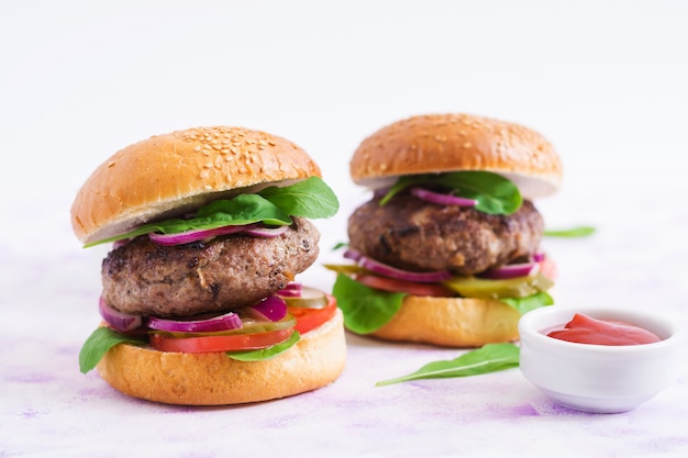 Großes Sandwich - Hamburgerburger mit Rindfleisch, Essiggurken, Tomate und roten Zwiebeln auf einem hellen Hintergrund.