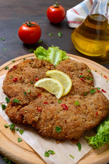 Großes Wiener Schnitzel auf einem Holzbrett mit Zitrone auf dunklem Hintergrund. Fleischgericht