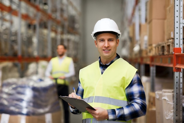 Foto großhandel, logistik, personal und exportkonzept - mann mit klemmbrett in reflektierender warnweste im lager