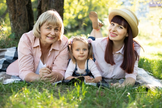 Großmutter, Mutter und Enkelin genießen sonnigen Gartenurlaub zusammen im Freien, liegen auf grünem Gras auf der Decke und lächeln. Freizeit-Familienlebensstil, Glück und Momente.