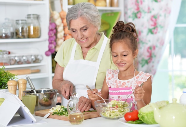 Großmutter und Enkelin bereiten Abendessen mit Tablet am Tisch zu