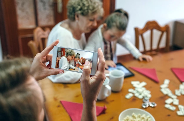 Großmutter und Enkelin spielen ein Spiel auf dem Tablet, während die Mutter ein Foto mit dem Smartphone macht. Selektive Fokussierung auf das Smartphone im Vordergrund
