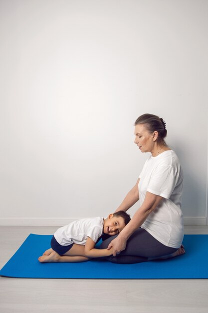 Großmutter und ihr Enkel sitzen auf einer Yogamatte in einer weißen Wohnung