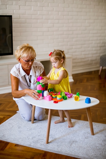 Großmutter und kleines Mädchen spielen mit Plastikblöcken im Raum