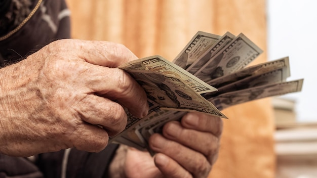 Großvater hält Geld in seinen Händen Ein älterer Mann zählt Dollar im Zimmer am Fenster