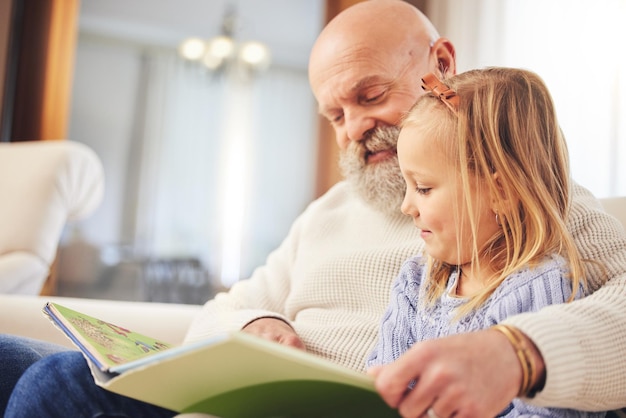 Großvater, Kind und Familie lesen auf dem Sofa im Wohnzimmer mit Liebe und Lernunterstützung. Glückliches Zuhause und Kind mit einem älteren Mann in einem Haus mit einem Märchenbuch und Jugenderziehung auf einer Couch